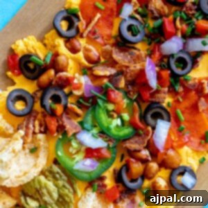 picture of pub cheese spread on a board covered with pork rinds, jalapenos, olives, bacon crumbles, peanuts, pimiento peppers, chives, red onion, and pepperoni