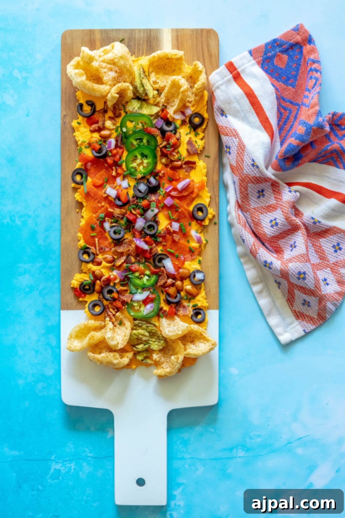 picture of pub cheese spread on a board covered with pork rinds, jalapenos, olives, bacon crumbles, peanuts, pimiento peppers, chives, red onion, and pepperoni