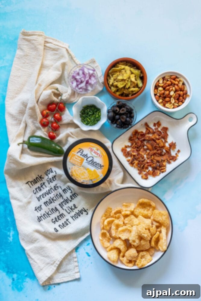 picture of pub cheese, pork rinds, jalapenos, olives, bacon crumbles, peanuts, pimiento peppers, chives, red onion, and pepperoni on a table