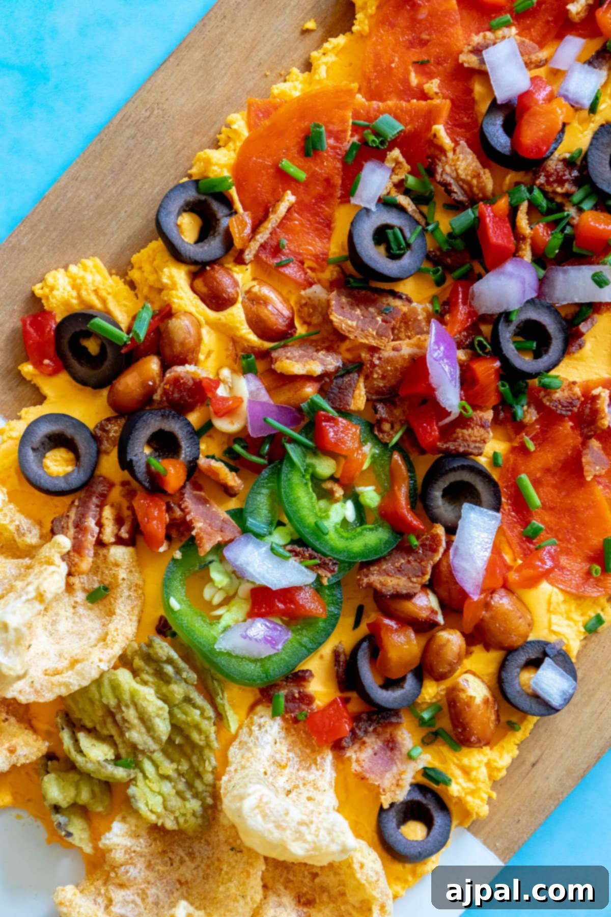 picture of pub cheese spread on a board covered with pork rinds, jalapenos, olives, bacon crumbles, peanuts, pimiento peppers, chives, red onion, and pepperoni