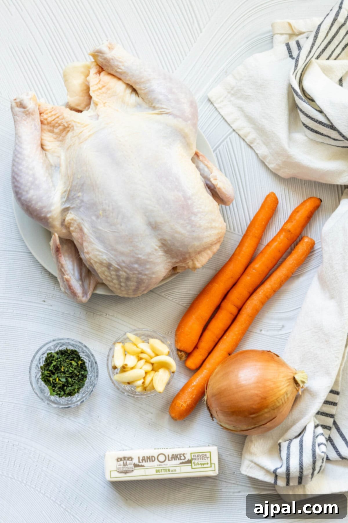 Effortless Perfect Roast Chicken 5 A whole roast chicken with carrots and onions on a white plate.