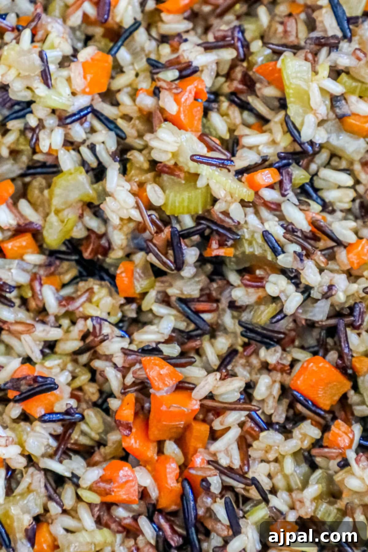 A close-up and inviting shot of wild rice pilaf, highlighting the distinct grains of wild rice perfectly mixed with vibrant pieces of celery, onions, and carrots.