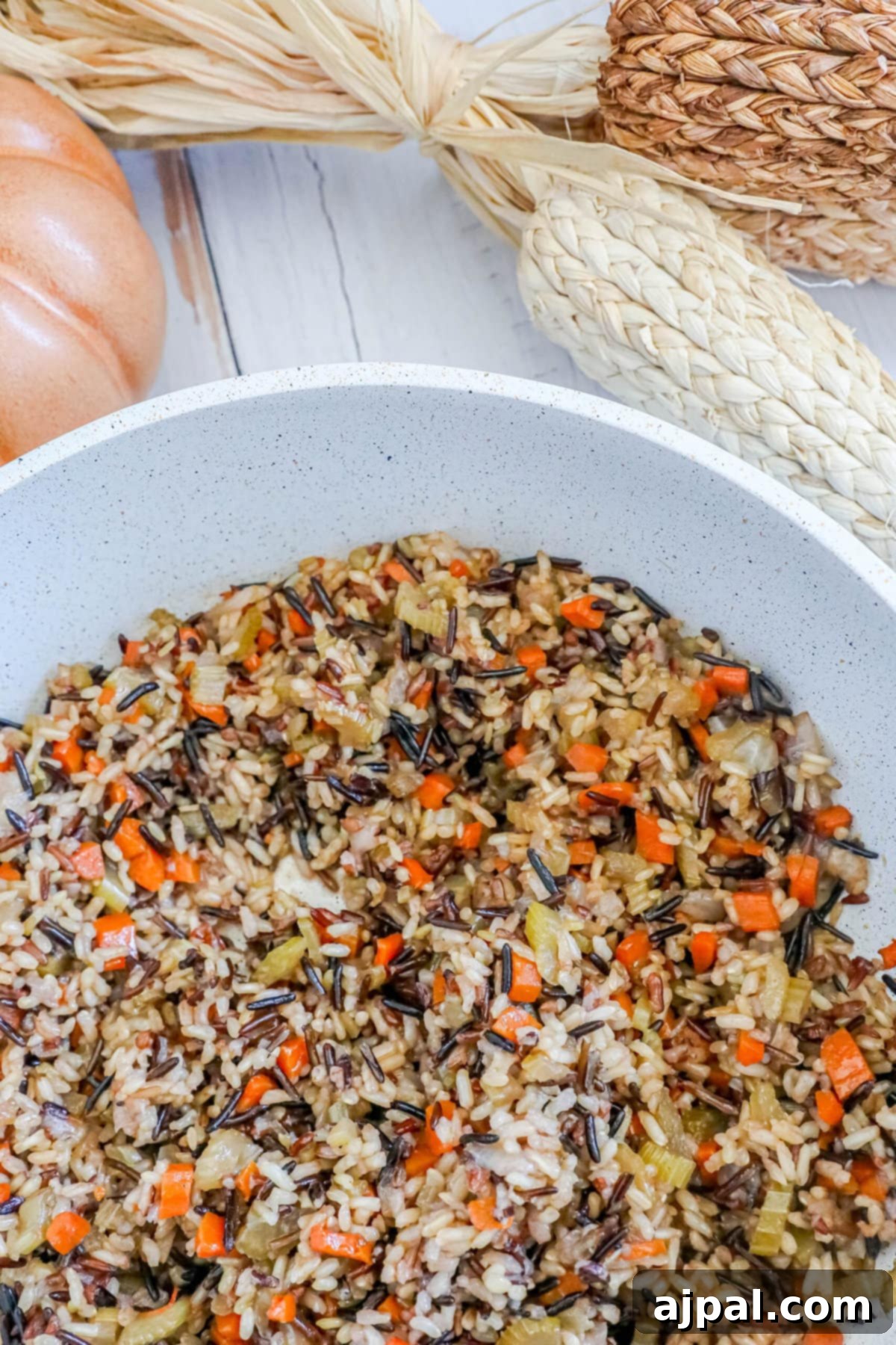 A beautiful presentation of wild rice pilaf, studded with colorful carrots, celery, and onions, artfully arranged in a rustic white pan on a wooden table, ready to be served.