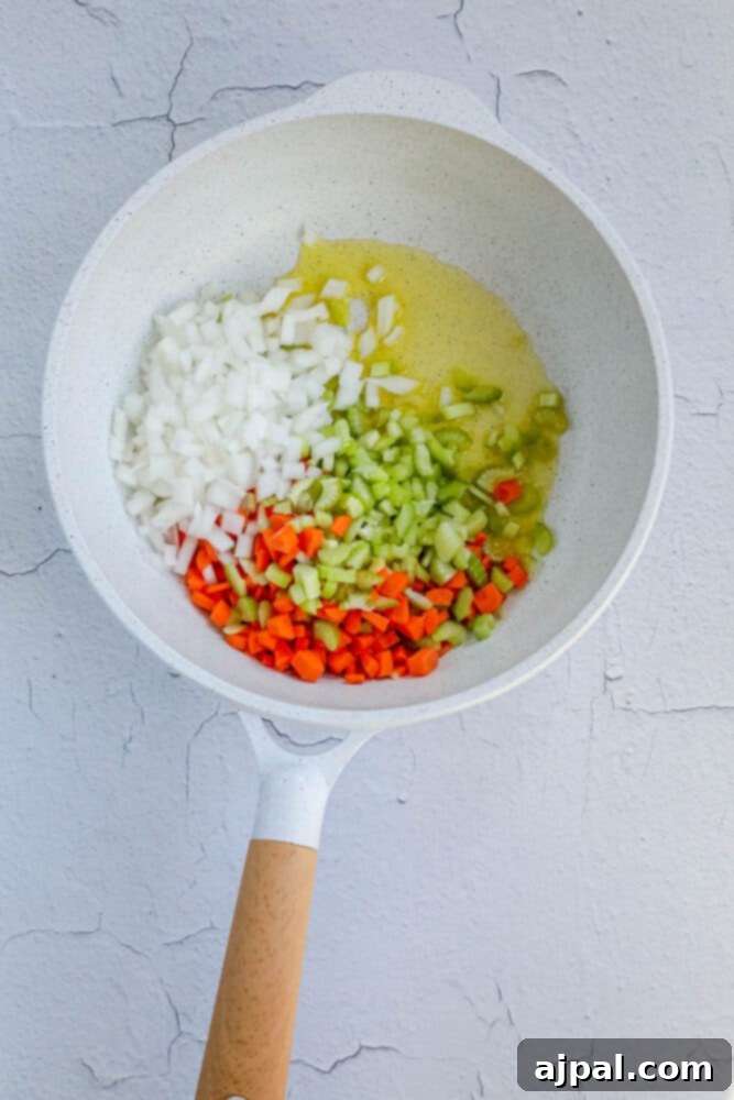 A culinary scene showing butter, finely diced onions, crisp celery, and vibrant carrots, all simmering gently in a pan, releasing their aromatic flavors for the wild rice pilaf.