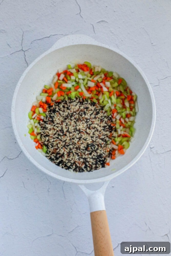 A delectable composition of golden oil, tender carrots, sweet onions, and nutty wild rice pilaf, all mingling harmoniously in a pan, toasting to perfection.