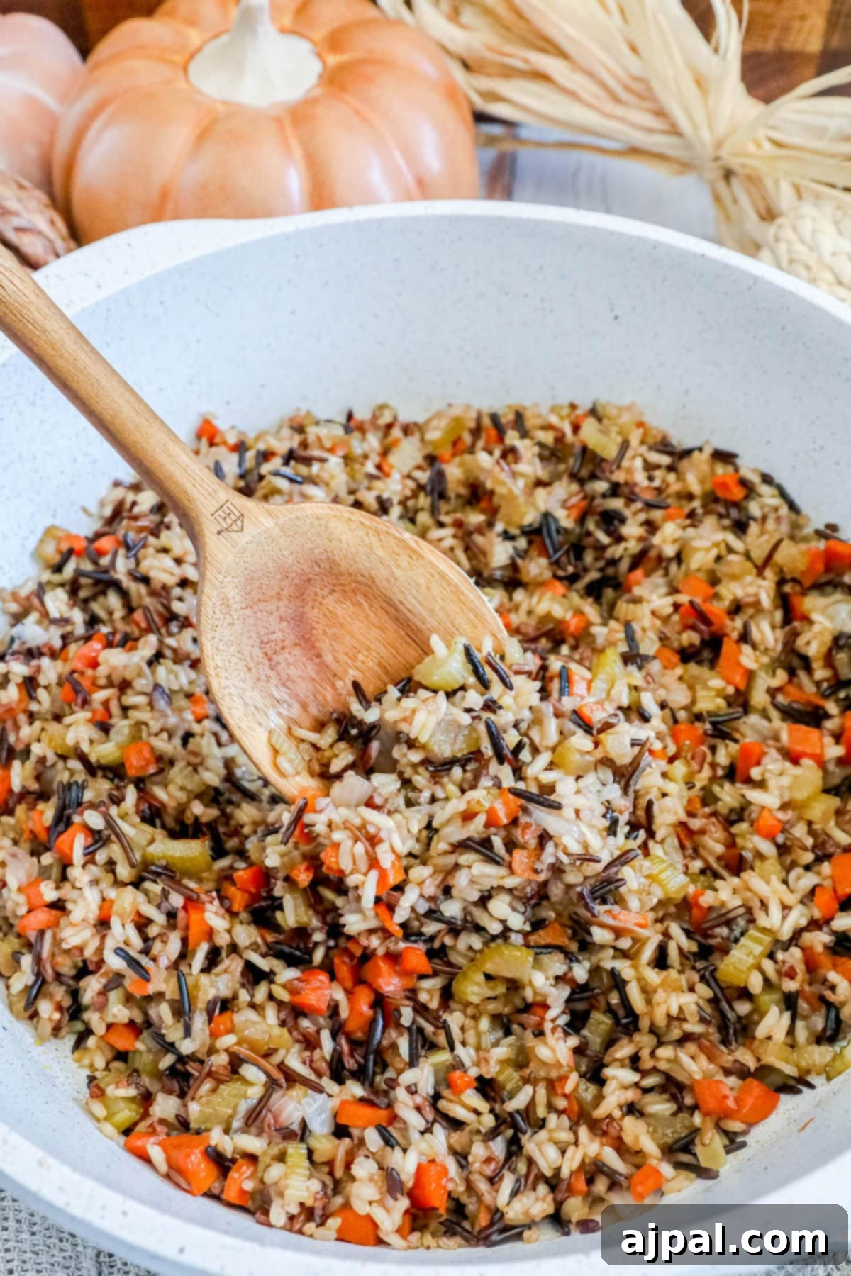 A classic white bowl brimming with fluffy wild rice pilaf, served with a wooden spoon for easy scooping, perfectly showcasing this delicious and comforting recipe.