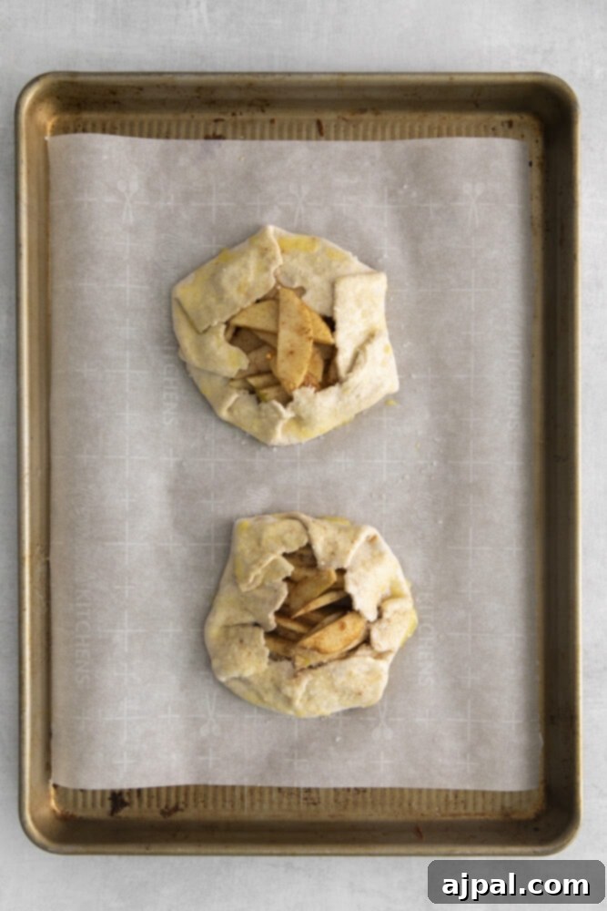 Two freshly baked apple galettes cooling on a baking sheet, their crusts golden and filling bubbling.