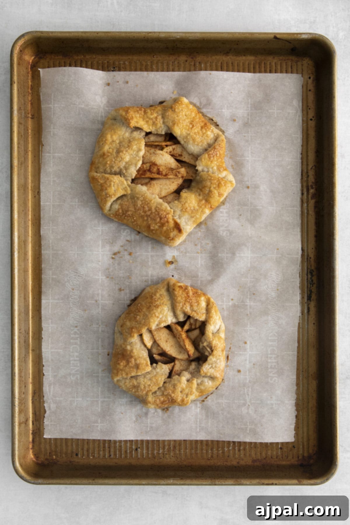 Two golden-brown apple galettes cooling on a parchment-lined baking sheet, their rustic edges and bubbling filling visible.