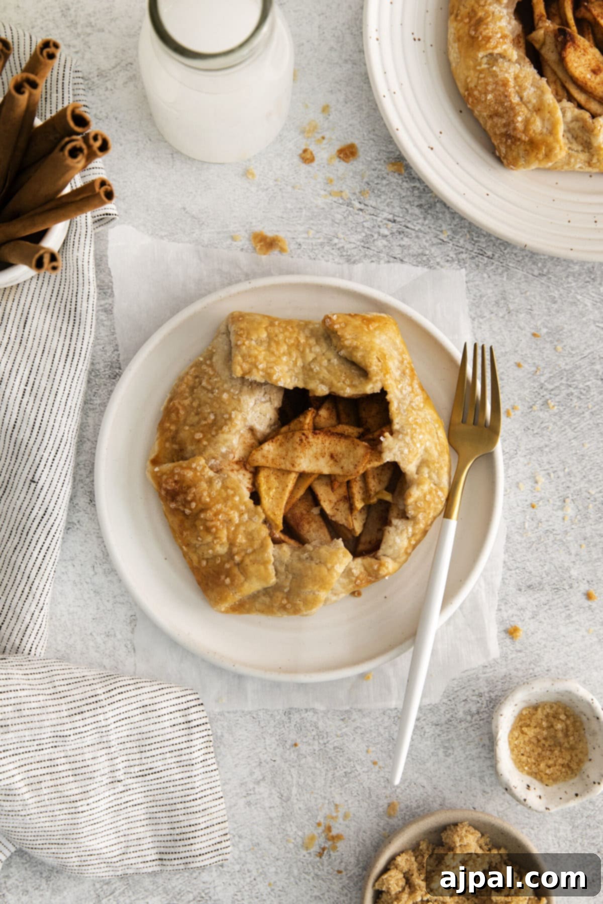 A homemade apple galette, beautifully arranged with cinnamon-infused apples, resting on a clean white plate with a fork.