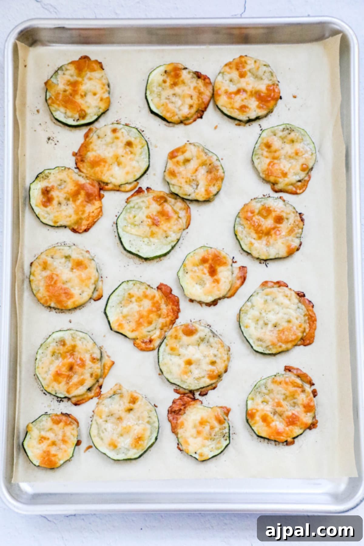 Parmesan Crusted Zucchini 8 picture of baked sliced zucchini with melted cheese on a baking sheet lined with parchment paper