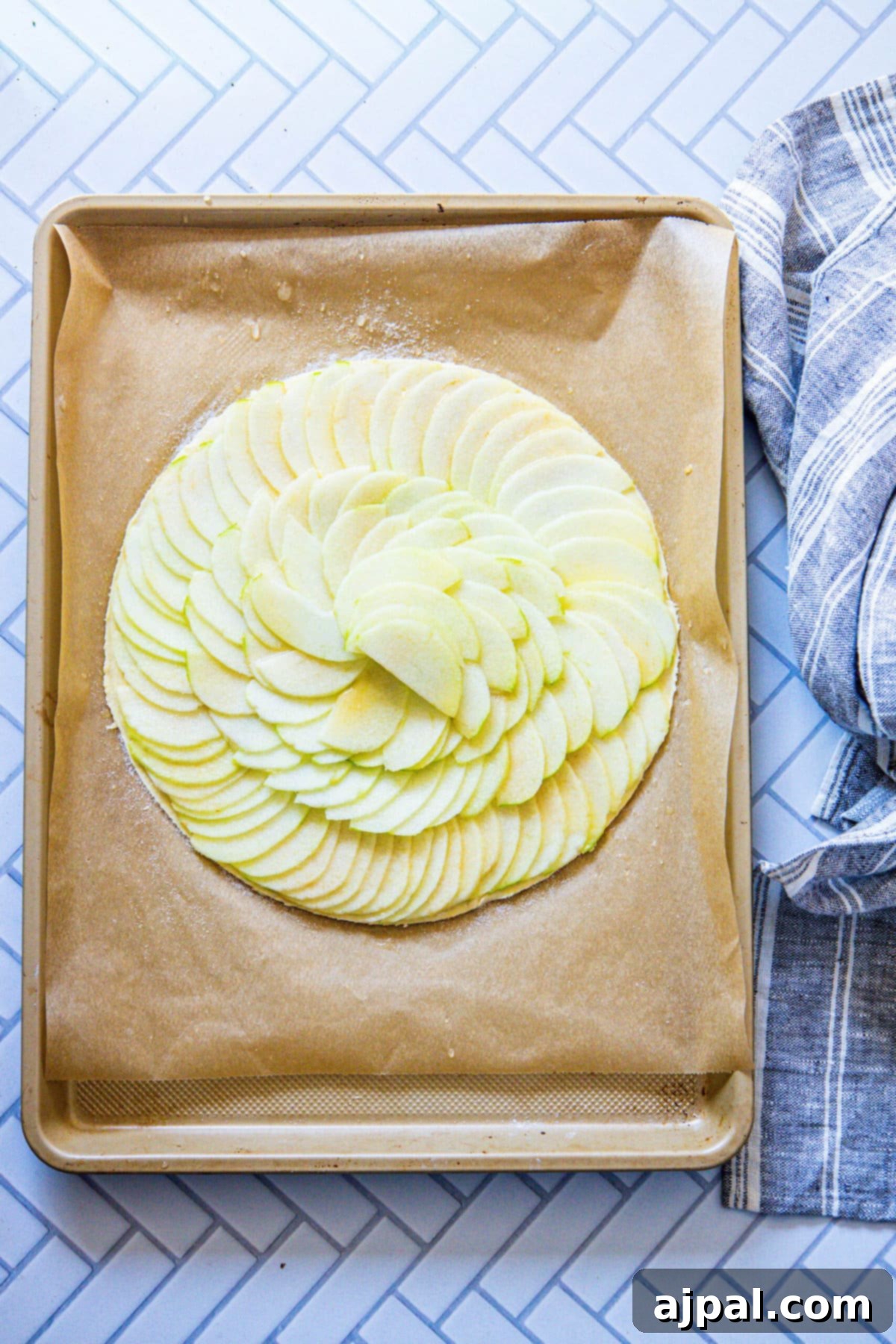 Simple Perfection: French Apple Tart 8 Expertly sliced apples, fanned out and arranged in an elegant, circular pattern on a baking sheet, forming the core of an Easy French Apple Tart before baking.