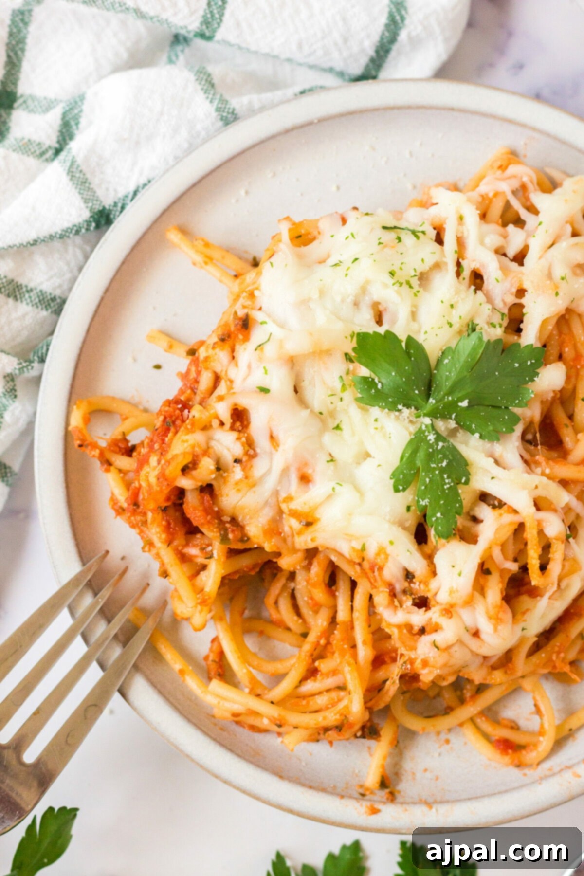 Ultimate Cheesy Spaghetti Bake 2 picture of baked spaghetti with melted cheese on a plate topped with basil with forks next to it