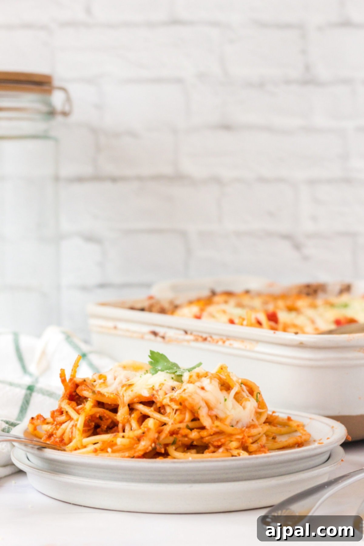Ultimate Cheesy Spaghetti Bake 11 picture of baked spaghetti with melted cheese on a plate topped with basil with forks next to it