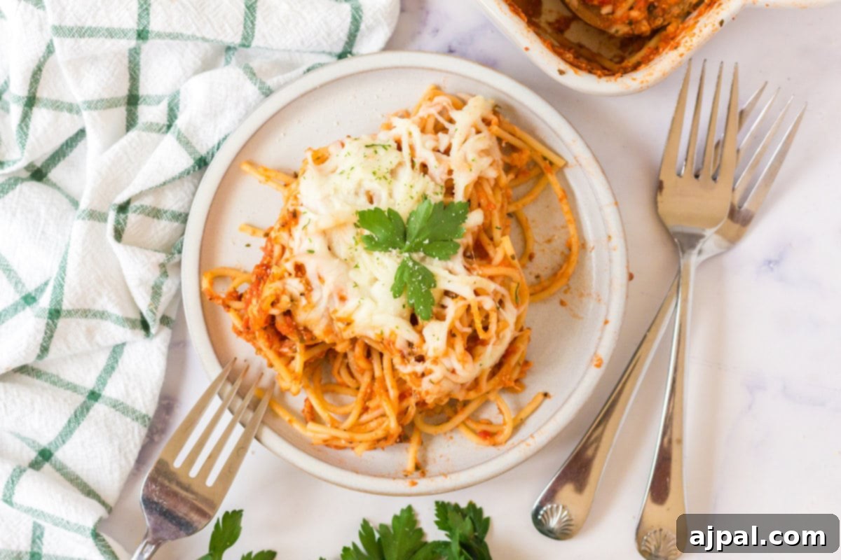 Ultimate Cheesy Spaghetti Bake 3 picture of baked spaghetti with melted cheese on a plate topped with basil with forks next to it