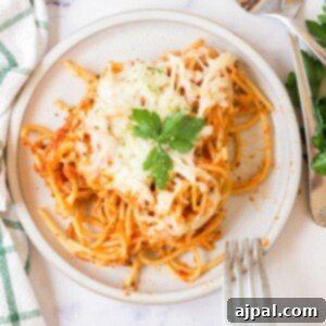 picture of baked spaghetti with melted cheese on a plate topped with basil with forks next to it