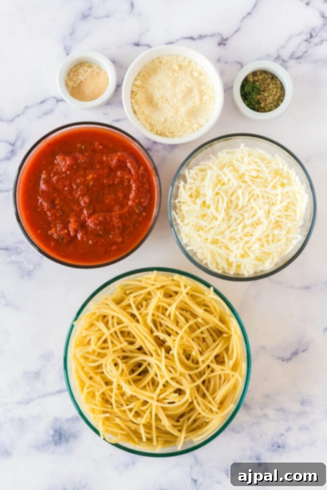 Ultimate Cheesy Spaghetti Bake 5 picture of spaghetti, pasta sauce in a bowl, shredded cheese in a bowl, parmesan cheese in a bowl, herbs and spices in a bowl on a table