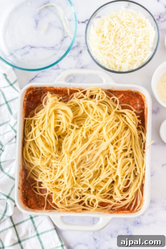 Ultimate Cheesy Spaghetti Bake 7 picture of spaghetti and pasta sauce in a white casserole dish being mixed