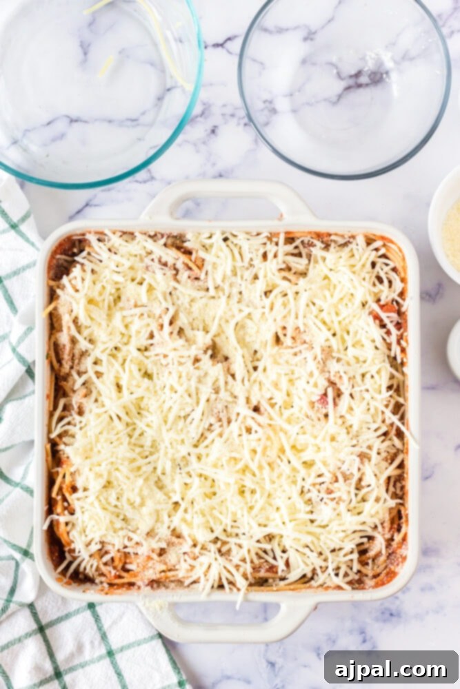Ultimate Cheesy Spaghetti Bake 8 picture of spaghetti in a casserole dish mixed with sauce and covered with shredded cheese