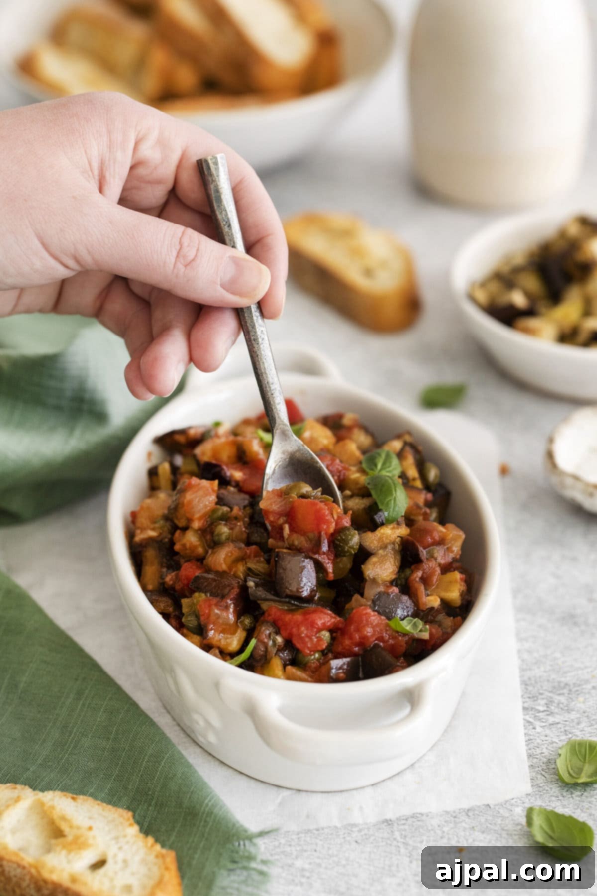 No-Fuss Eggplant Caponata 11 A close-up shot of a beautifully prepared vegan eggplant caponata in a white dish, garnished with fresh basil leaves, ready to be enjoyed.
