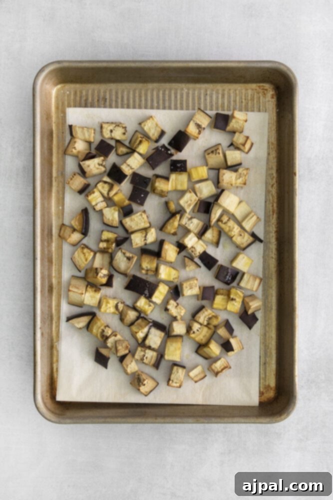 No-Fuss Eggplant Caponata 6 Golden-brown and tender roasted cubed eggplant pieces are scattered across a baking sheet lined with parchment paper, having achieved perfect caramelization.