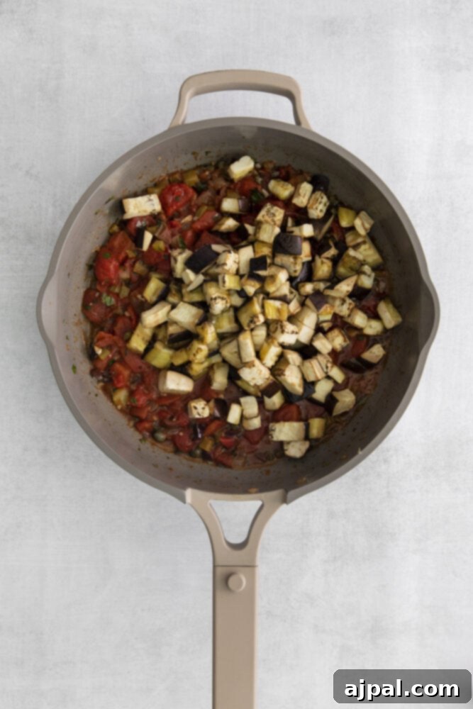 No-Fuss Eggplant Caponata 9 The roasted eggplant cubes are gently incorporated into the simmering tomato sauce, mingling with the browned vegetables and herbs in a large pan, ready to meld their flavors.
