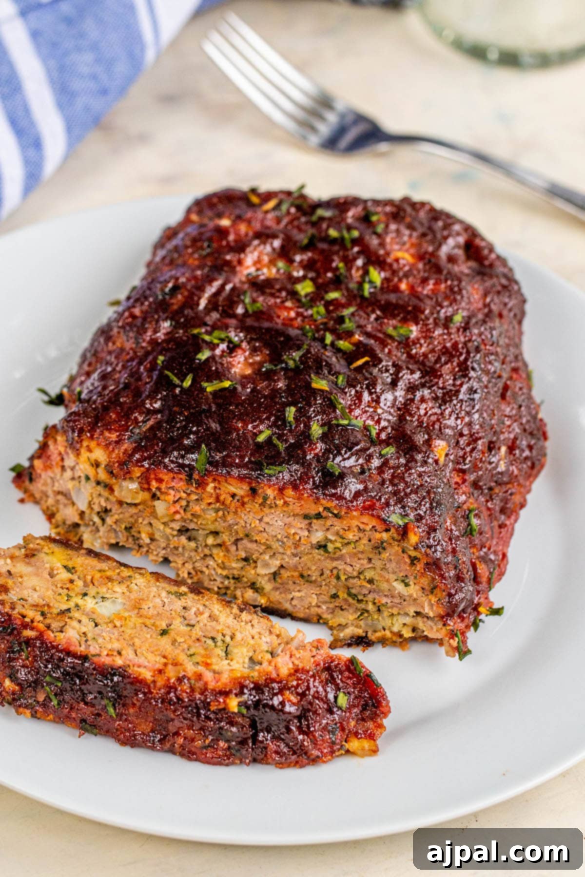 Smoked meatloaf on a white plate with one slice sliced, showcasing its perfect texture and rich color.
