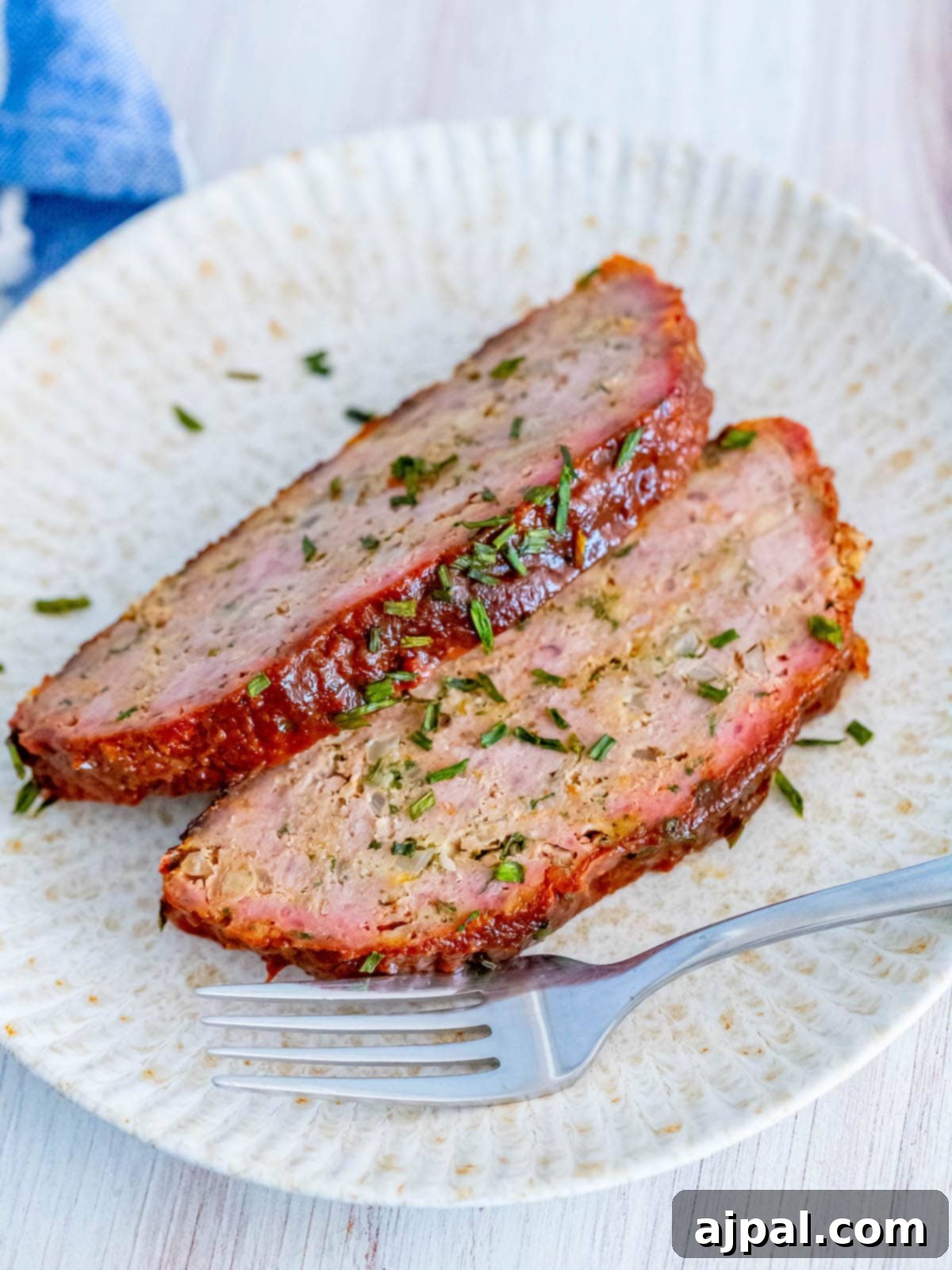 Two slices of smoked meatloaf on a white plate with basil garnish, highlighting the succulent interior.