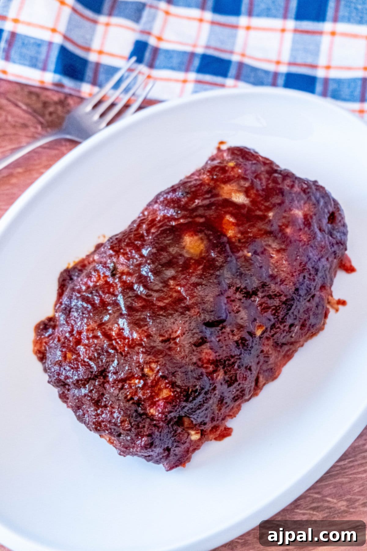 A perfectly smoked meatloaf on a white plate, showcasing its golden-brown glaze and inviting aroma.