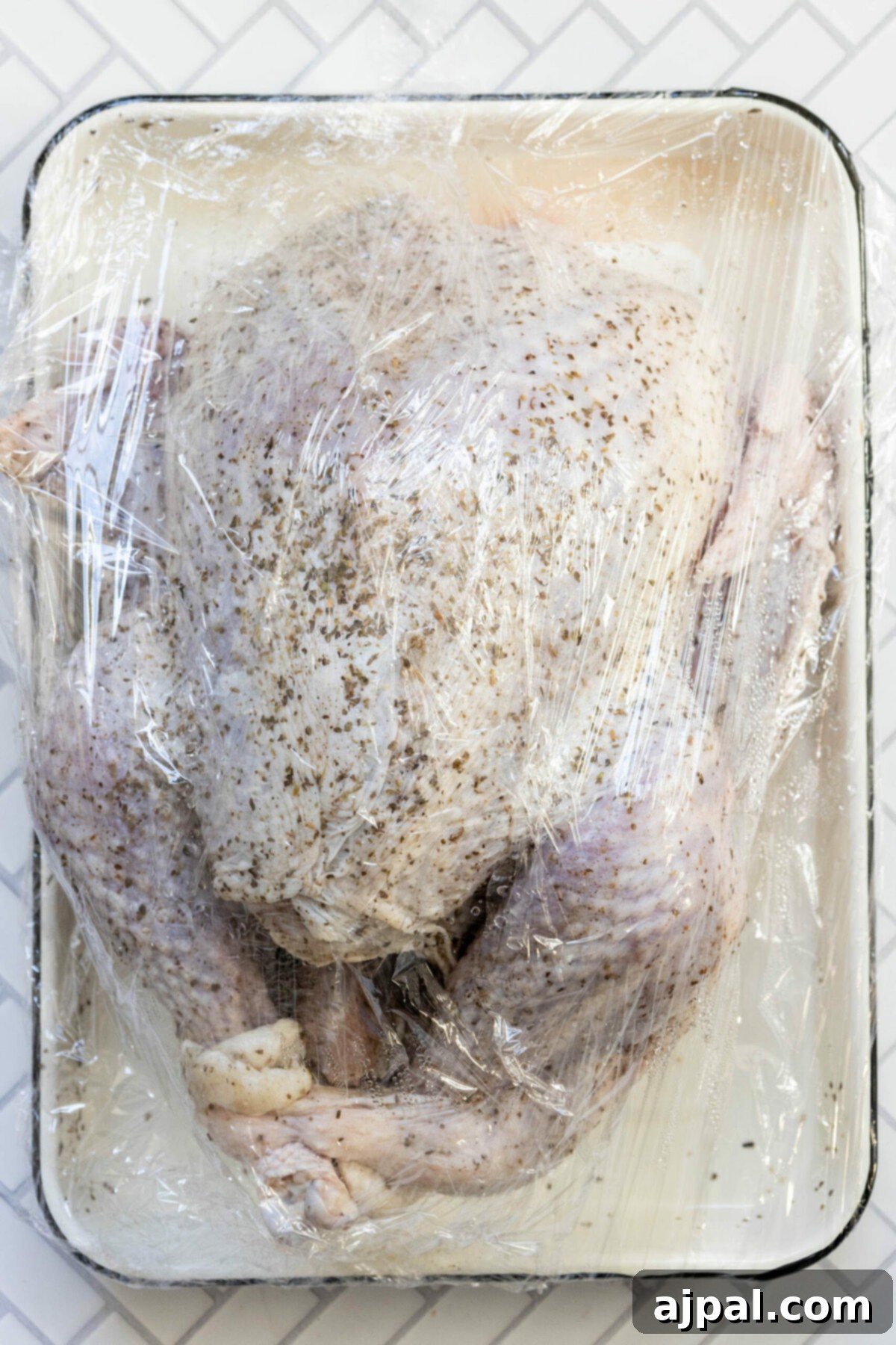 picture of turkey dry brining in plastic wrap on a white tray