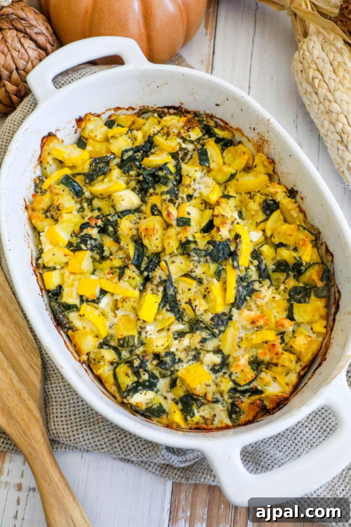 Green & Gold Feta Casserole 2 A beautifully baked spinach, zucchini, and feta casserole in a white ceramic dish, ready to be served on a rustic wooden table.