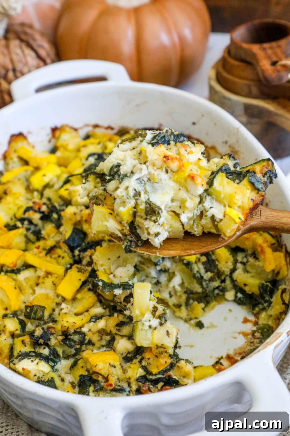 Green & Gold Feta Casserole 12 A serving spoon lifting a portion of the cheesy spinach and zucchini feta casserole, highlighting its creamy texture.