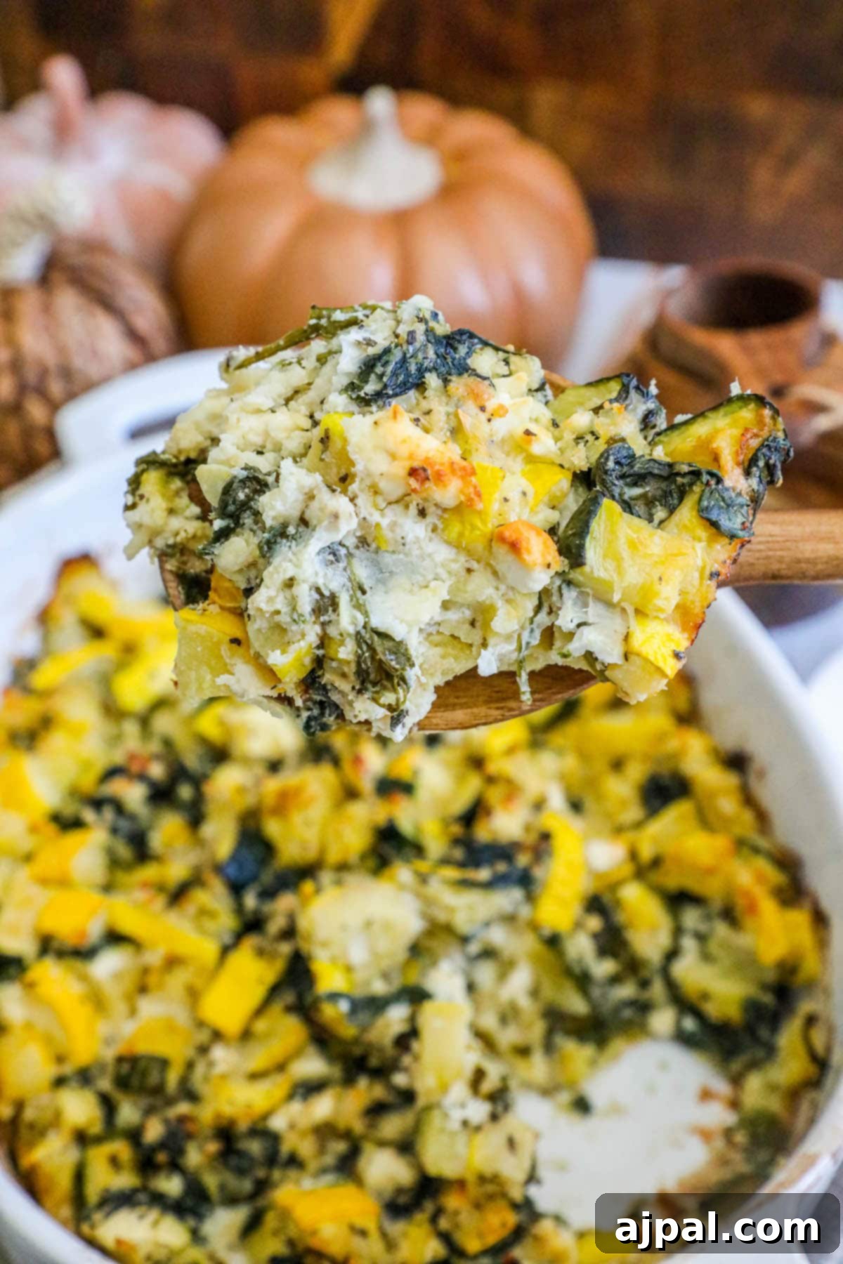 Green & Gold Feta Casserole 13 A wooden spoon rests in a white dish filled with baked spinach, zucchini, and feta casserole, invitingly warm and ready to eat.