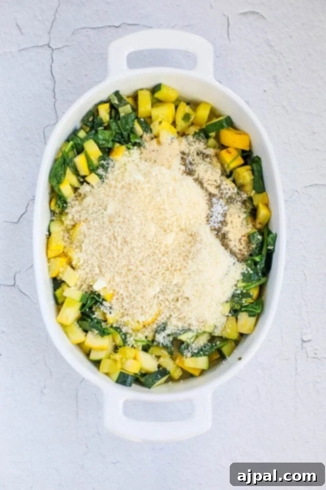 Green & Gold Feta Casserole 7 Sautéed squash and spinach mixture in a white casserole dish, being topped with breadcrumbs and cheese before baking.