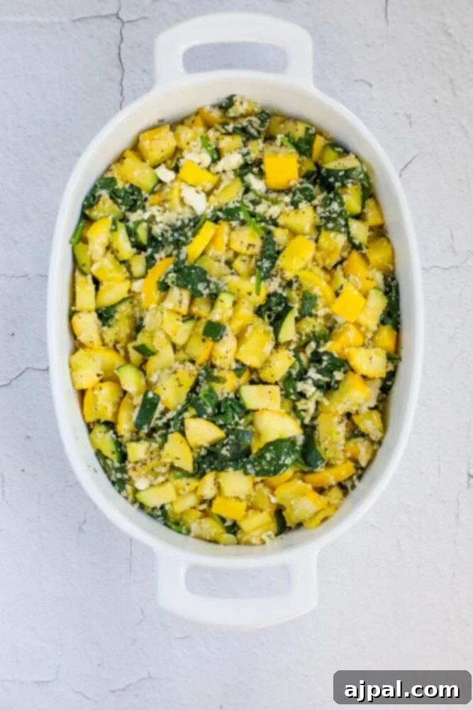 Green & Gold Feta Casserole 8 An unbaked mixed squash casserole, vibrant with vegetables and cheese, prepared in a white baking dish before going into the oven.