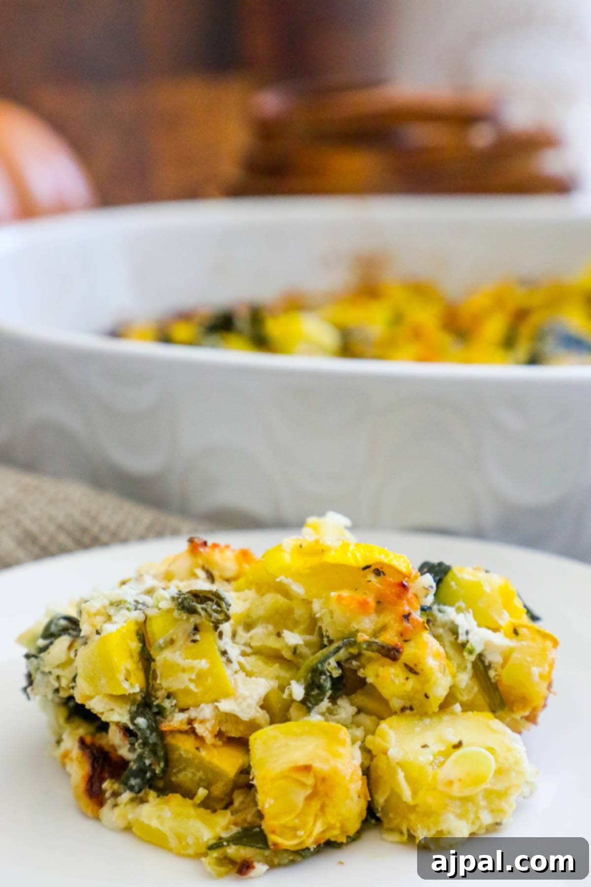 Green & Gold Feta Casserole 10 A generous scoop of yellow and zucchini squash casserole, rich with spinach and feta, presented on a white plate.