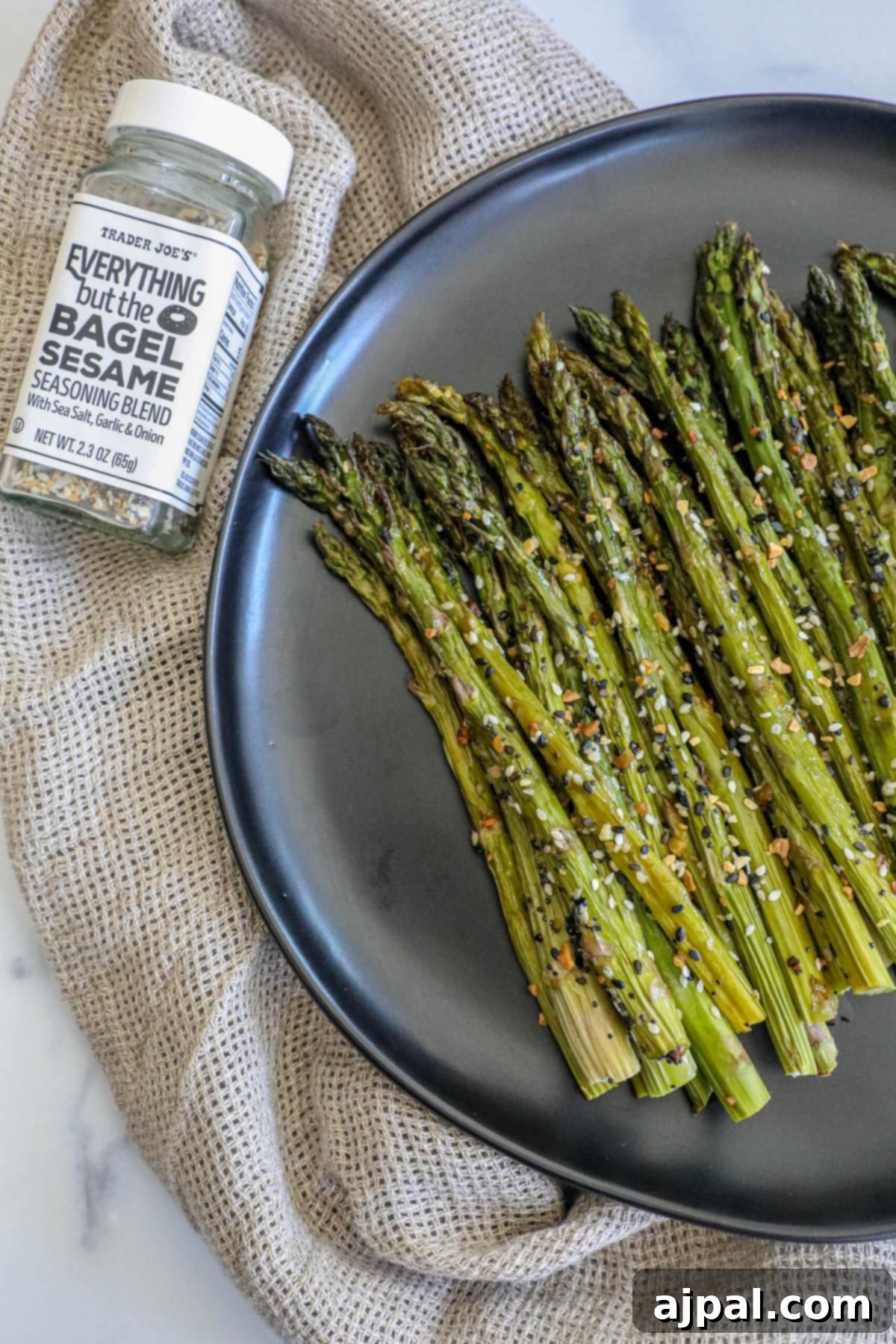 Crispy roasted asparagus spears generously coated with everything bagel seasoning on a black plate, showcasing the vibrant green and the contrasting seeds.