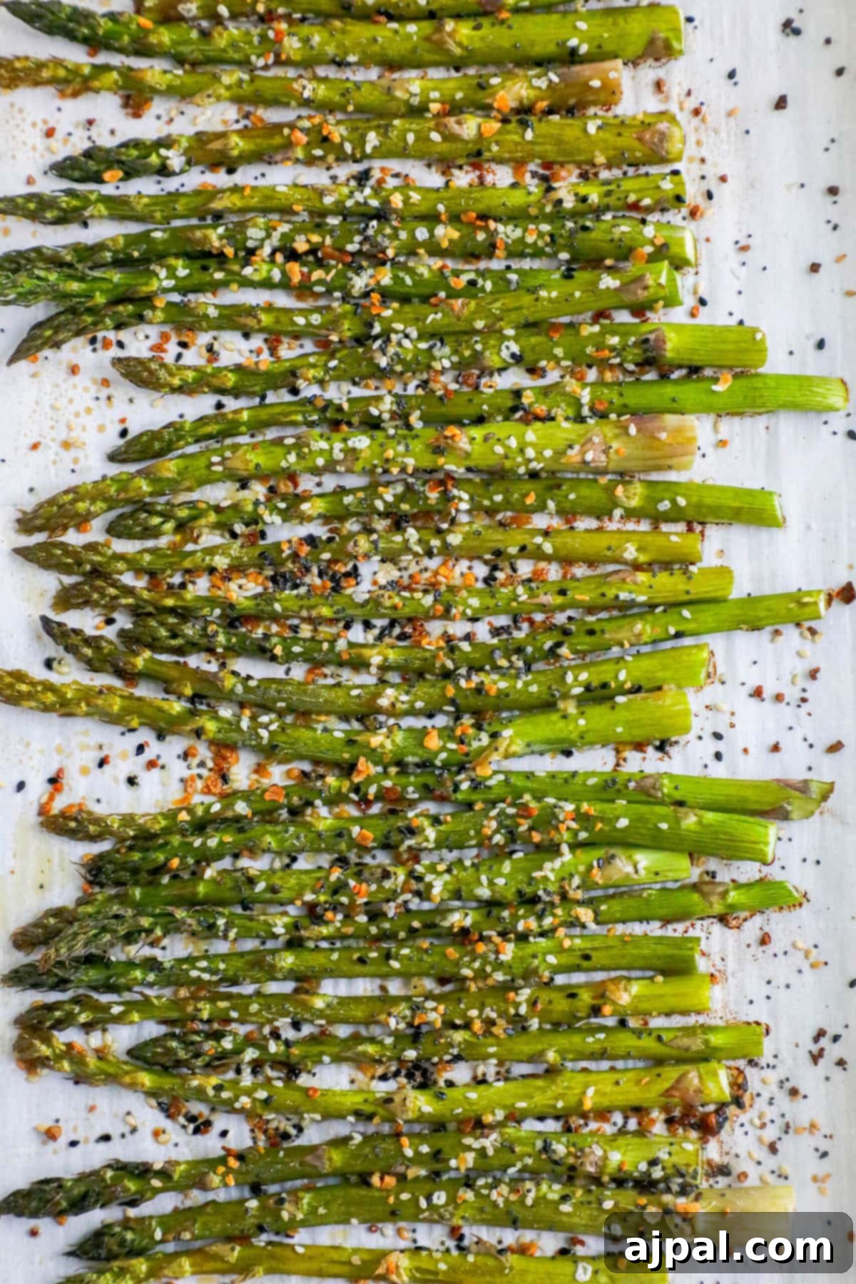 Close-up of roasted asparagus spears seasoned with everything bagel spice on a dark plate.