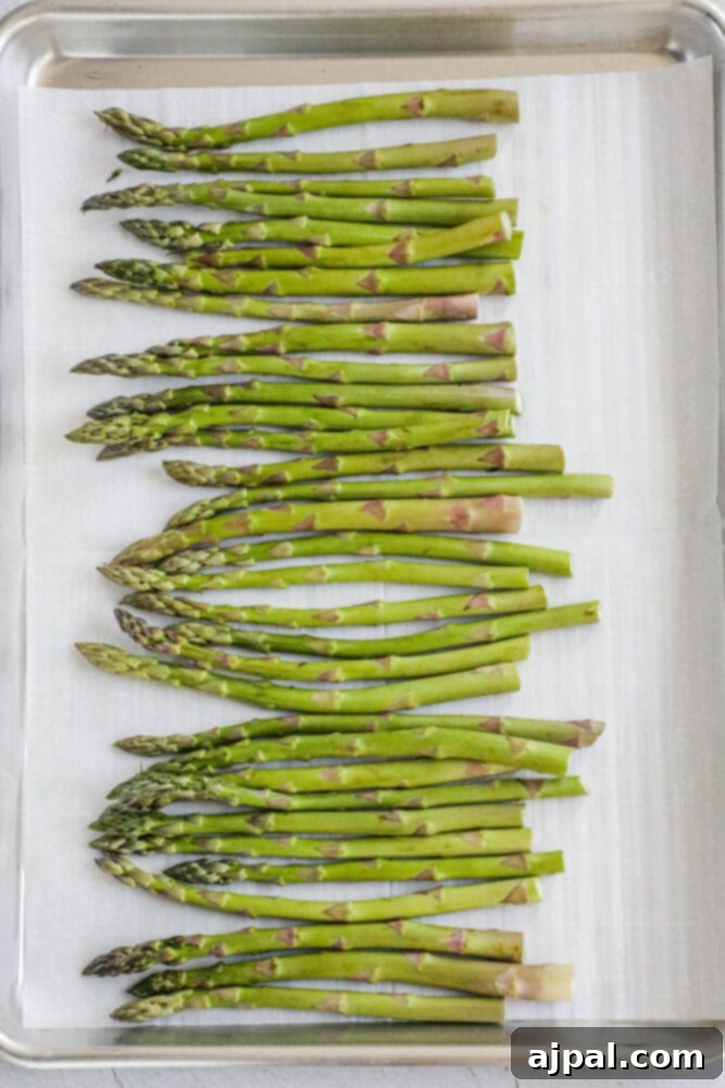 Picture of trimmed asparagus spears neatly arranged on a baking sheet lined with parchment paper.