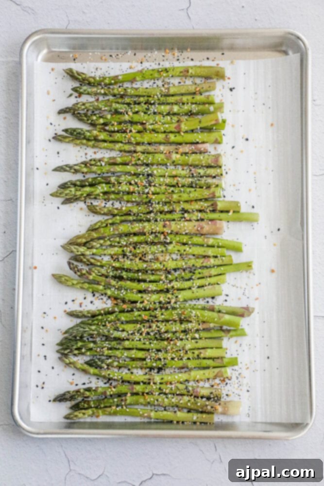 Close-up of asparagus with seasoning on a baking sheet before roasting.