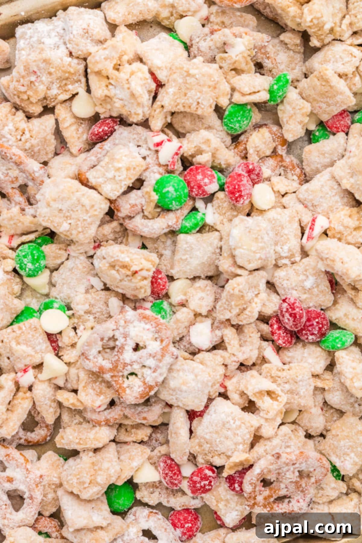 picture of muddy buddies chex mix with pretzels and red and green candies mixed in coated in powdered sugar