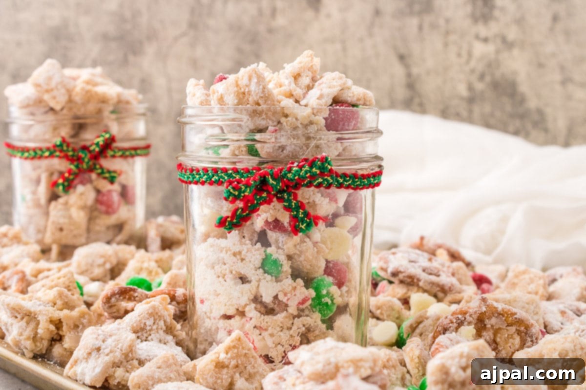 picture of muddy buddies chex mix with pretzels and red and green candies mixed in coated in powdered sugar in a jar with a red and green bow on it 
