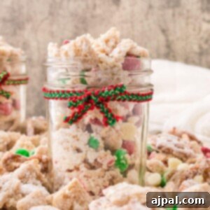 picture of muddy buddies chex mix with pretzels and red and green candies mixed in coated in powdered sugar in a jar with a red and green bow on it