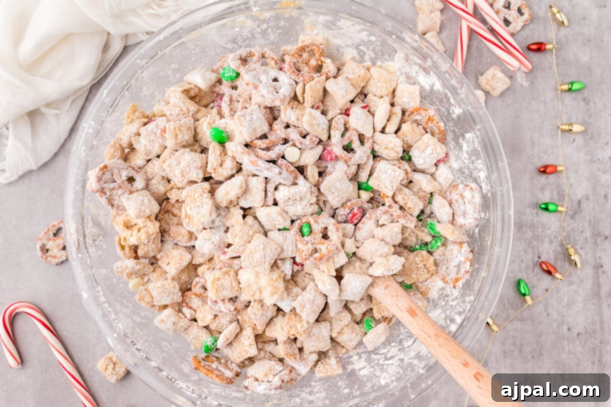picture of muddy buddies chex mix with pretzels and red and green candies mixed in coated in powdered sugar
