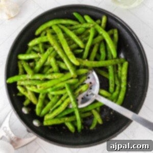 Picture of green beans sautéed with garlic and herbs in a pan with a spoon on a table