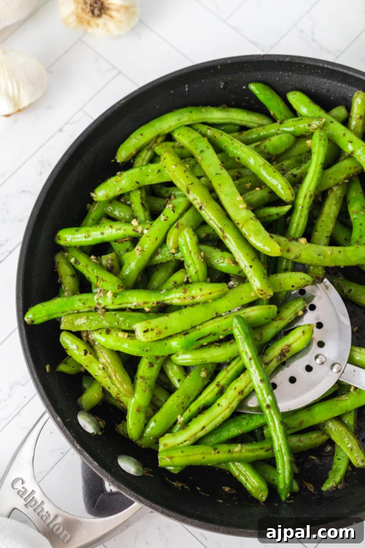 Green beans sautéed with garlic and herbs in a pan with a wooden spoon on a rustic table.