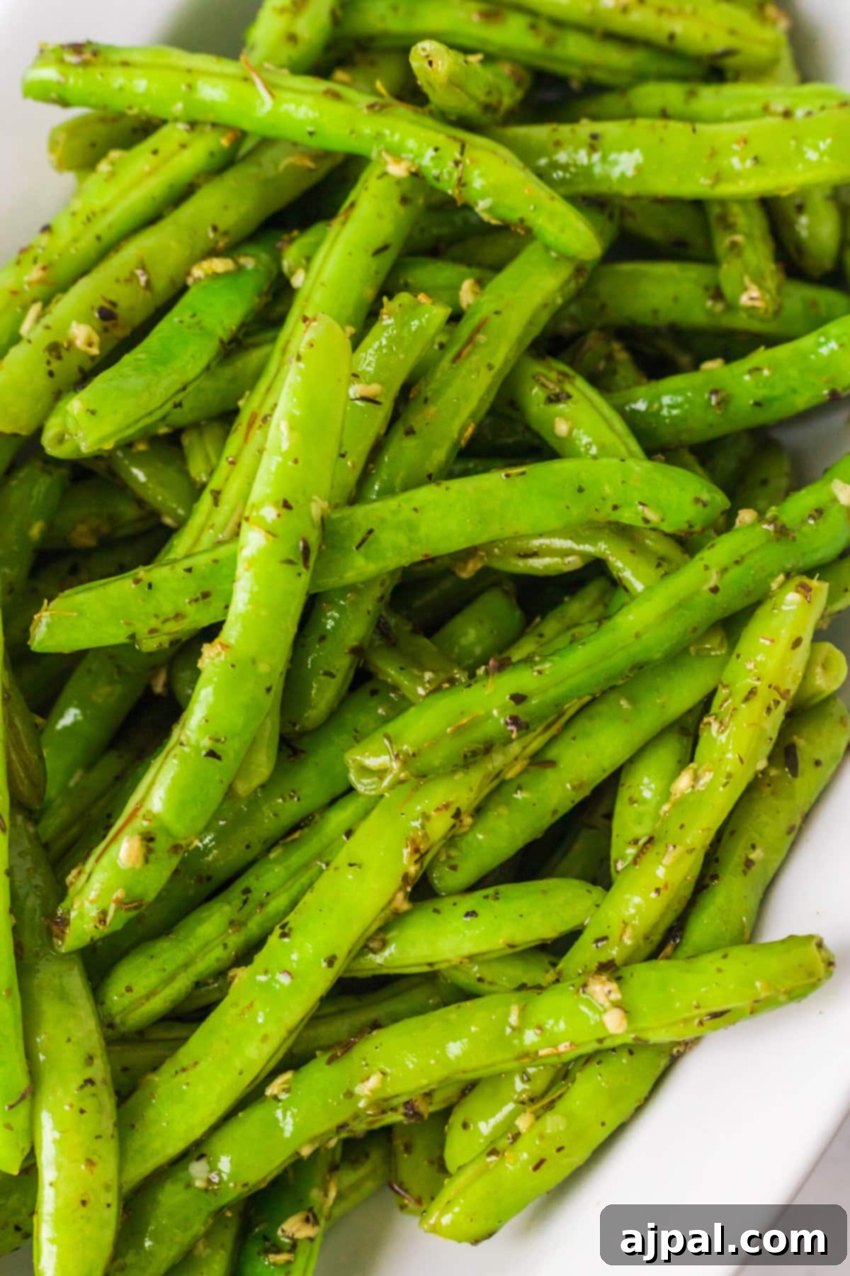 A serving of green beans seasoned with garlic and herbs in a white bowl.