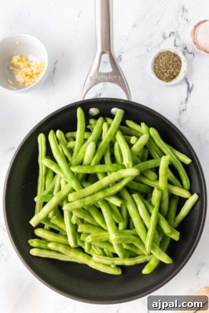 A close-up of garlic herb green beans, perfectly sautéed, in a pan.