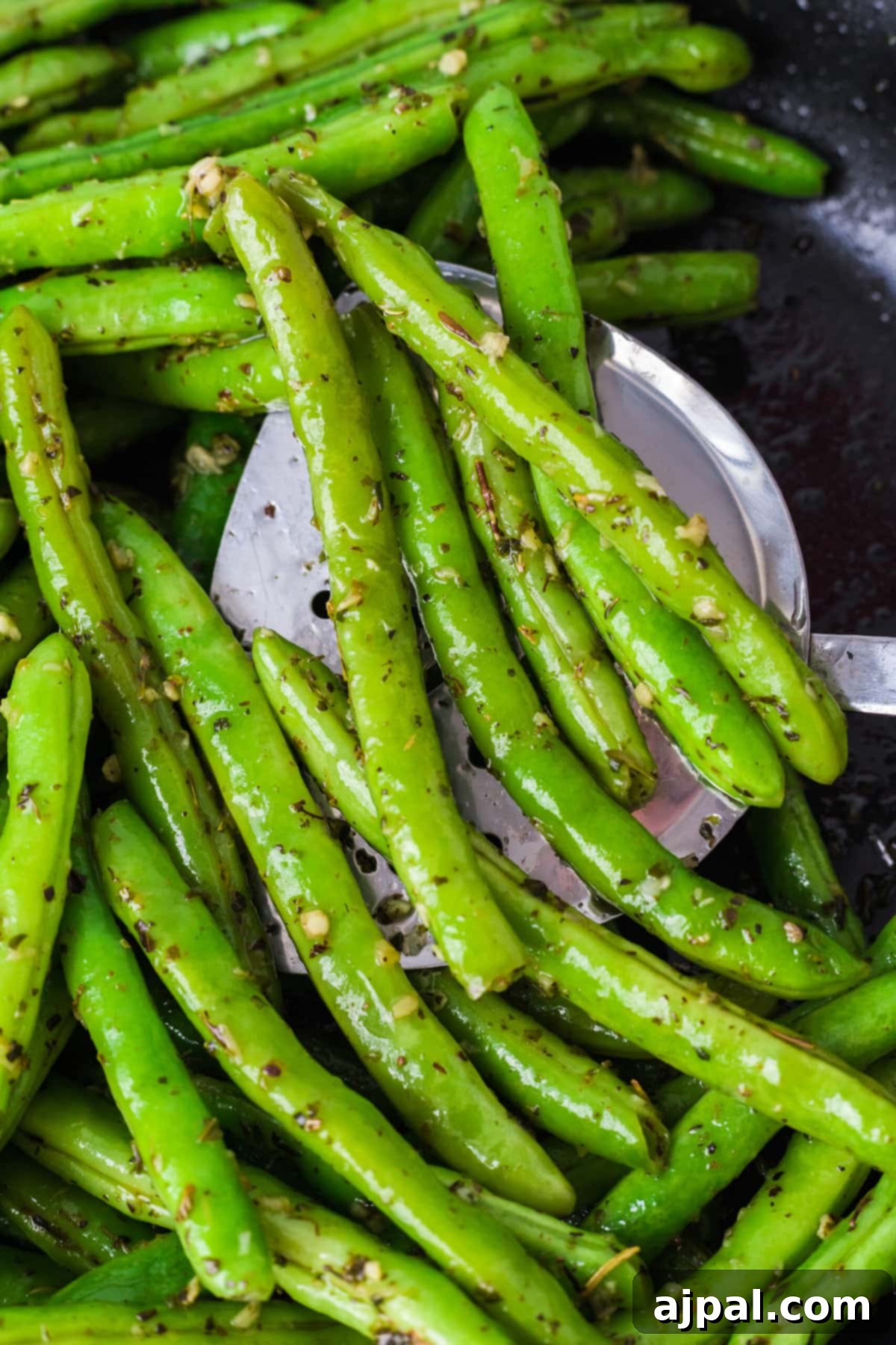 Garlic herb green beans actively sautéing in a skillet with a spatula for stirring.