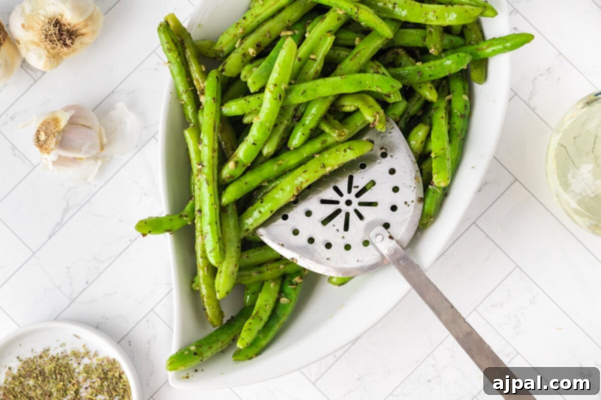 A large white bowl filled with garlic herb green beans, garnished with fresh herbs.