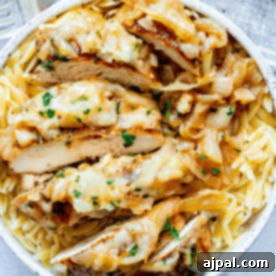 Classic French Onion Chicken Breasts 13 A plate of pasta topped with sliced baked French onion chicken, caramelized onions, and melted cheese, garnished with chopped parsley.